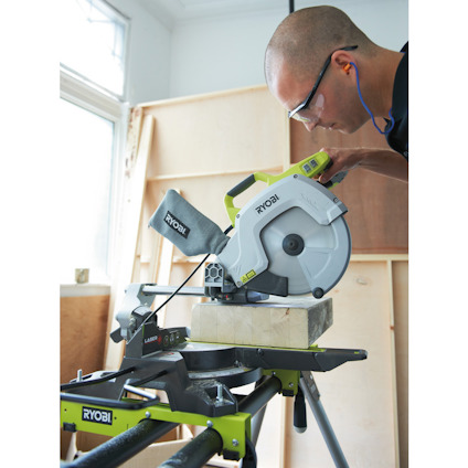 Person använder en Ryobi kap- och geringssåg på träblock, med hörselskydd och skyddsglasögon.