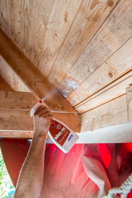 Arm sprayar träbjälkar och plankor med Mögel-Fri.