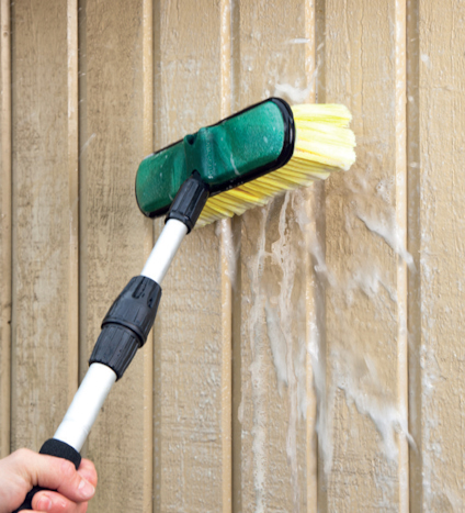 Hand håller borste med gul borst mot vertikala väggpaneler med rinnande vatten.