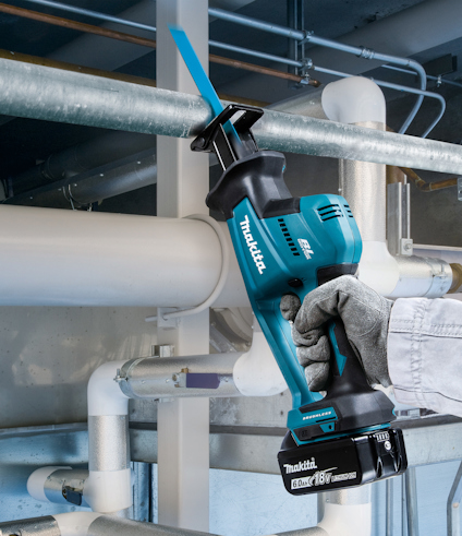 Person håller en blå Makita 18V batteridriven såg som skär genom ett metallrör.