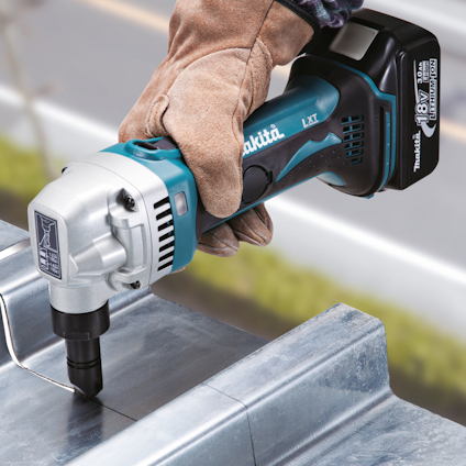 En person använder en blå och svart kraftsax för metall, märkt “Makita 18V LXT”. Hände skyddas av en arbetshandske.