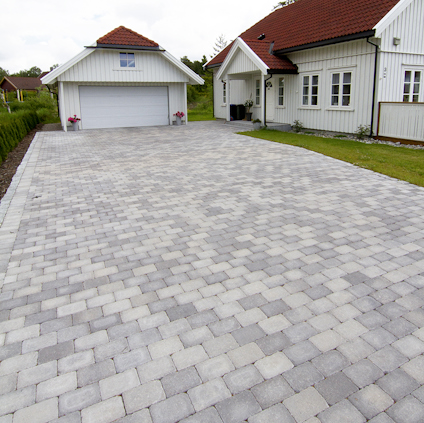 Uppfart av ljusgrå rektangulära stenar framför ett vitmålat hus med rött tak och garage.