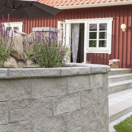 Stenmur med lavendelblommor framför ett träfasadhus med röd färg och vita knutar.