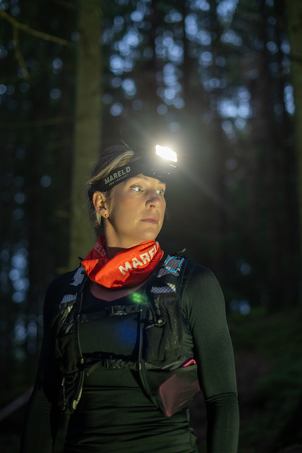 En person med pannlampa och röd halsduk i en skog om natten.