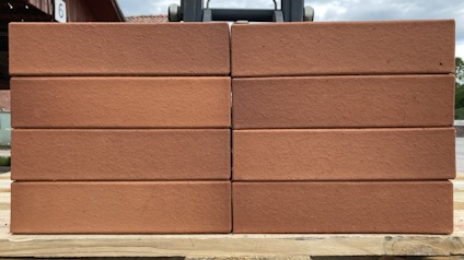 Rader av släta röda tegelstenar staplade på en träpall utomhus.