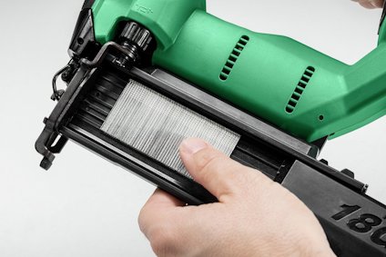 Person laddar en grön spikpistol med en rad metallspikar i en svart magasin.
