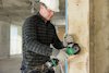 Person med hjälm och skyddsglasögon använder en vinkelslip på betongvägg, gnistor flyger.