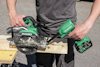 Person använder en grön batteridriven HiKOKI cirkelsåg för att såga en träplanka.