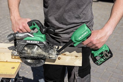 Person använder en grön batteridriven HiKOKI cirkelsåg för att såga en träplanka.