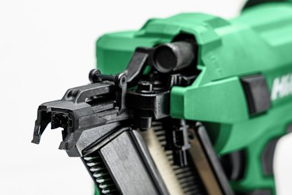Grön spikpistol med svart detaljer, laddad med metallspikar, på vit bakgrund.